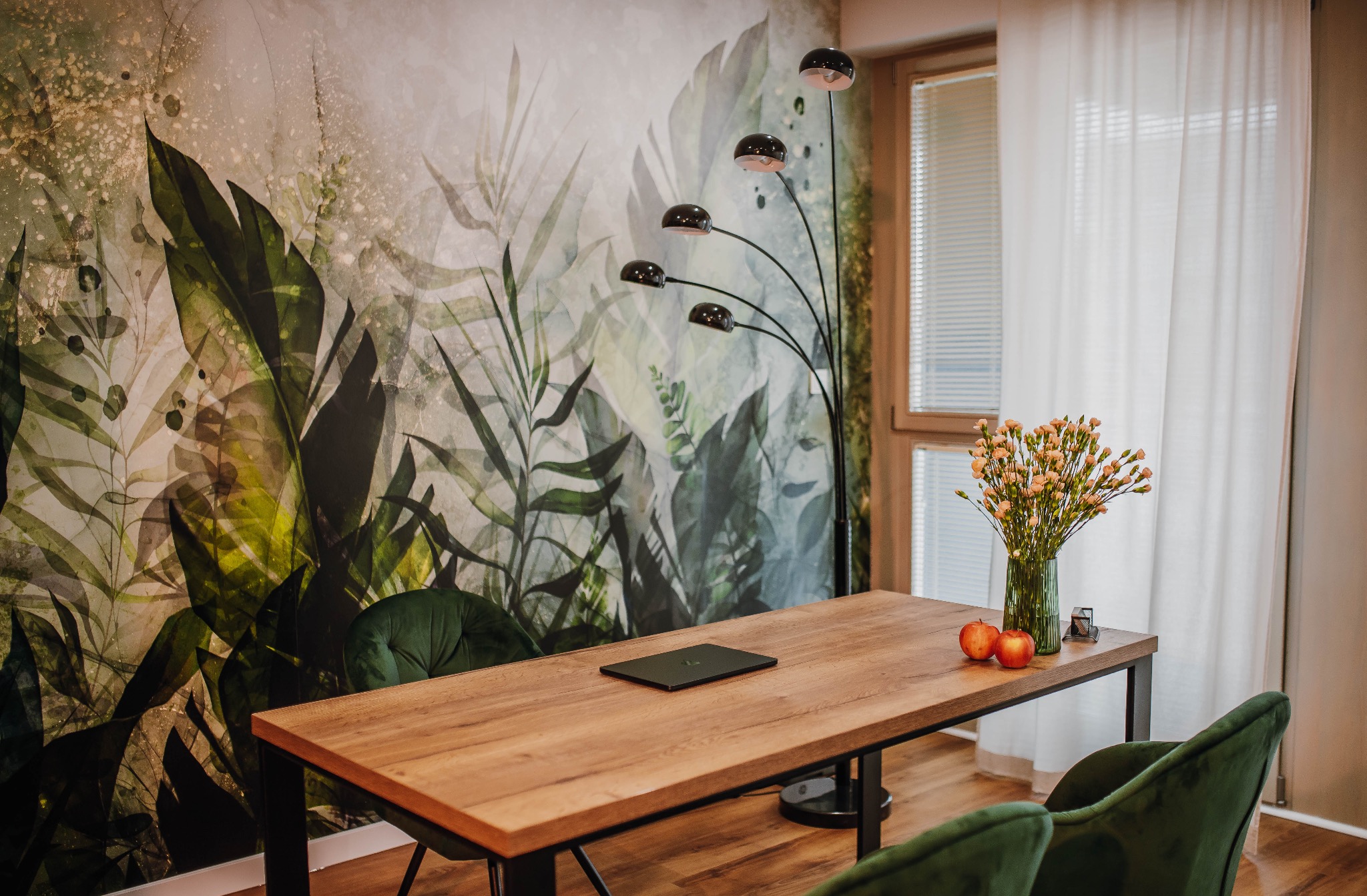 Gabinet w Łowiczu z biurkiem, laptopem, kwiatami w wazonie i tapetą w motywy roślinne, oświetlony lampą z pięcioma kloszami.