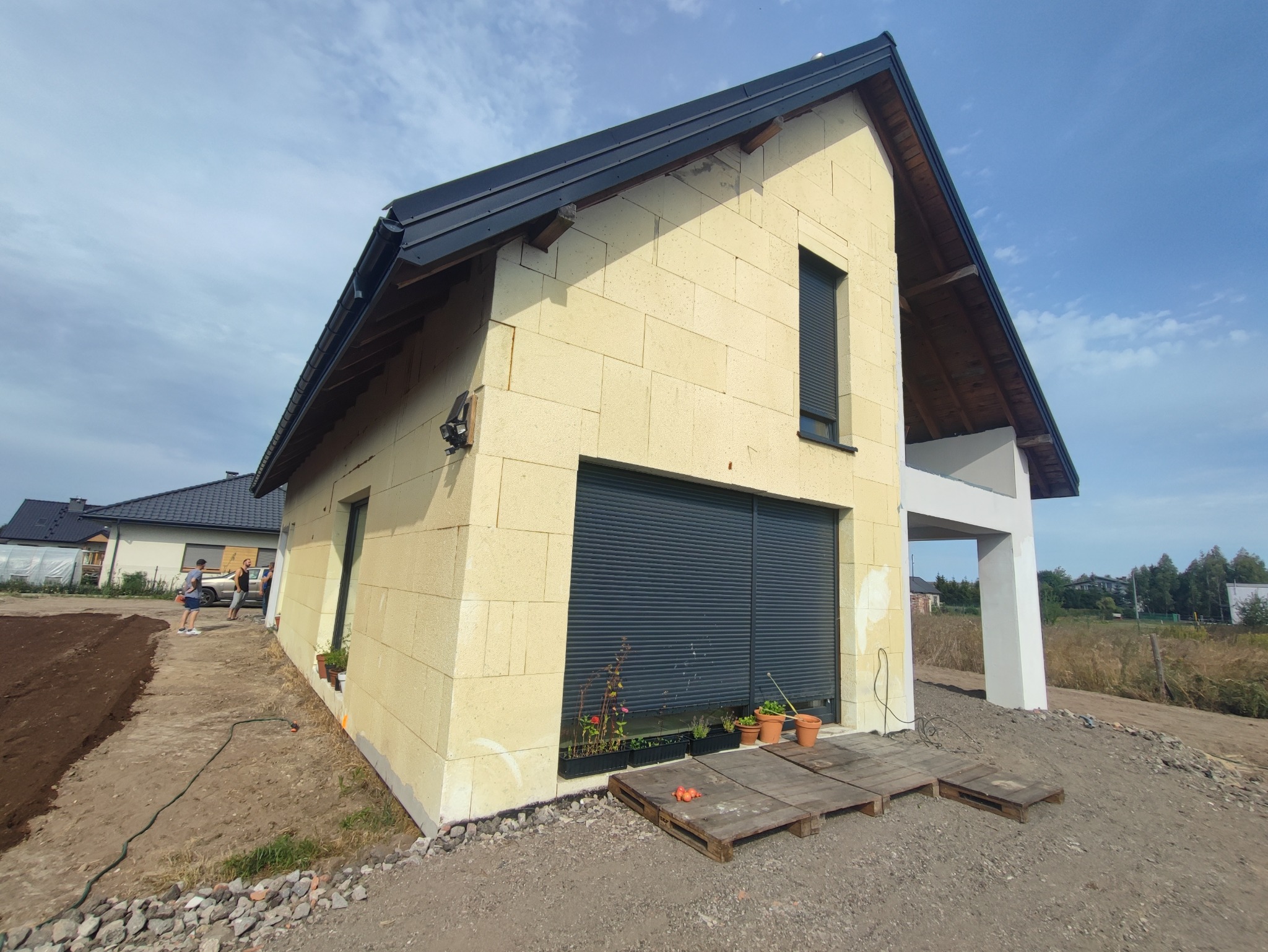 Surowy stan domu z bloczków betonu komórkowego Ytong, z zamontowanymi roletami zewnętrznymi, widok z zewnątrz na tle błękitnego nieba z chmurami.