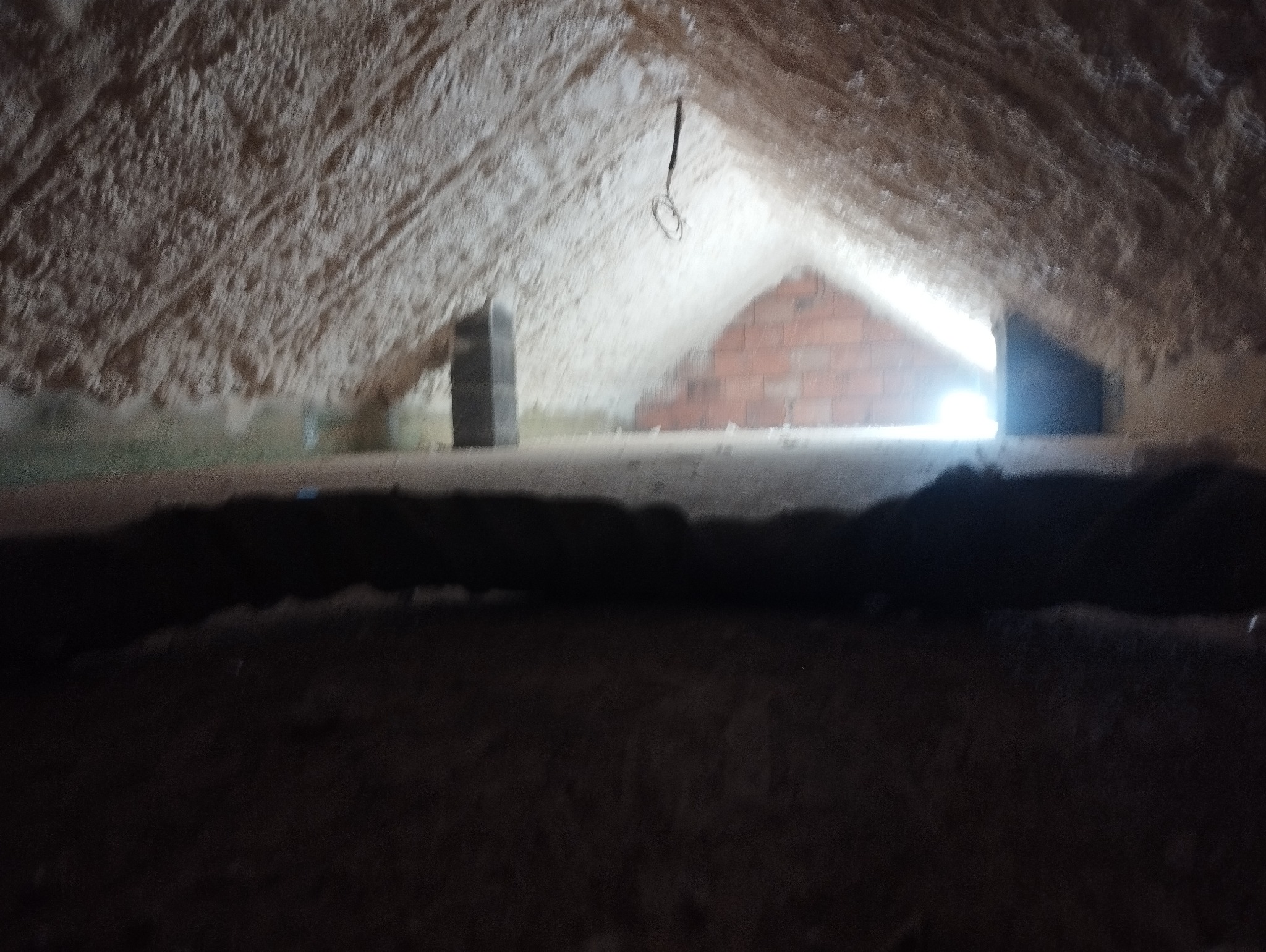 Poddasze po ociepleniu pianką PUR, widoczne ściany i dach pokryte grubą warstwą pianki, fragment muru z cegły w tle, ciemny element konstrukcyjny na pierwszym planie.