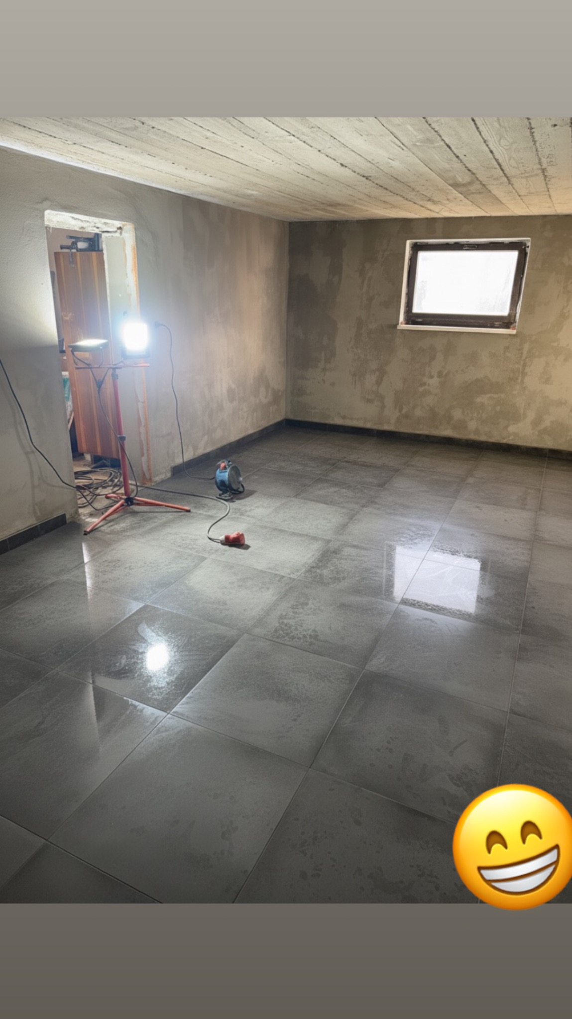 Wykończone podłogi z szarych płytek w pokoju w trakcie remontu. Widoczne narzędzia, lampa oświetleniowa i surowe ściany przygotowane do dalszych prac wykończeniowych.