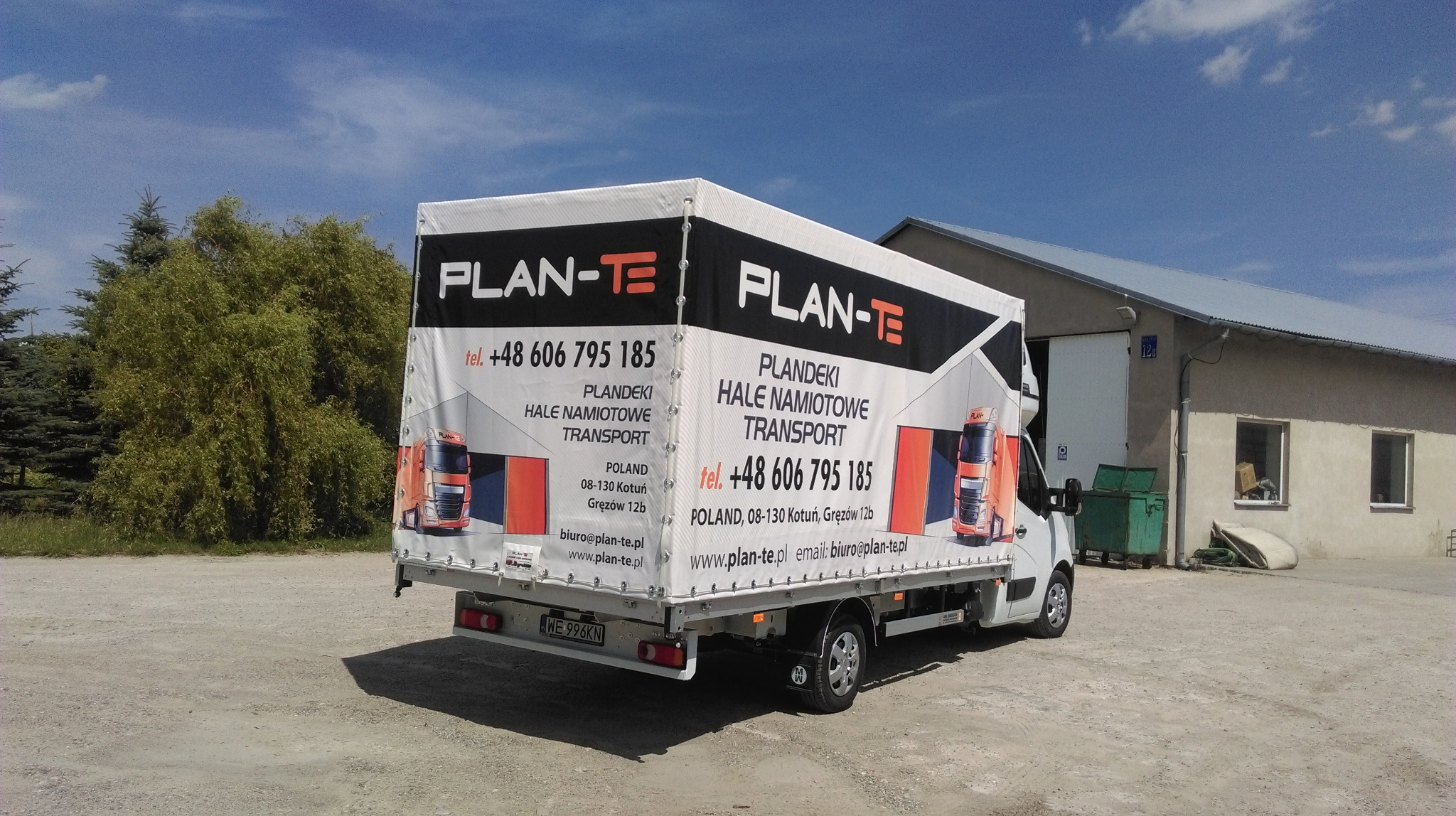 Biała ciężarówka z plandeką z nadrukiem reklamowym firmy Plan-Te, widok z tyłu na tle szarego budynku i drzew.
