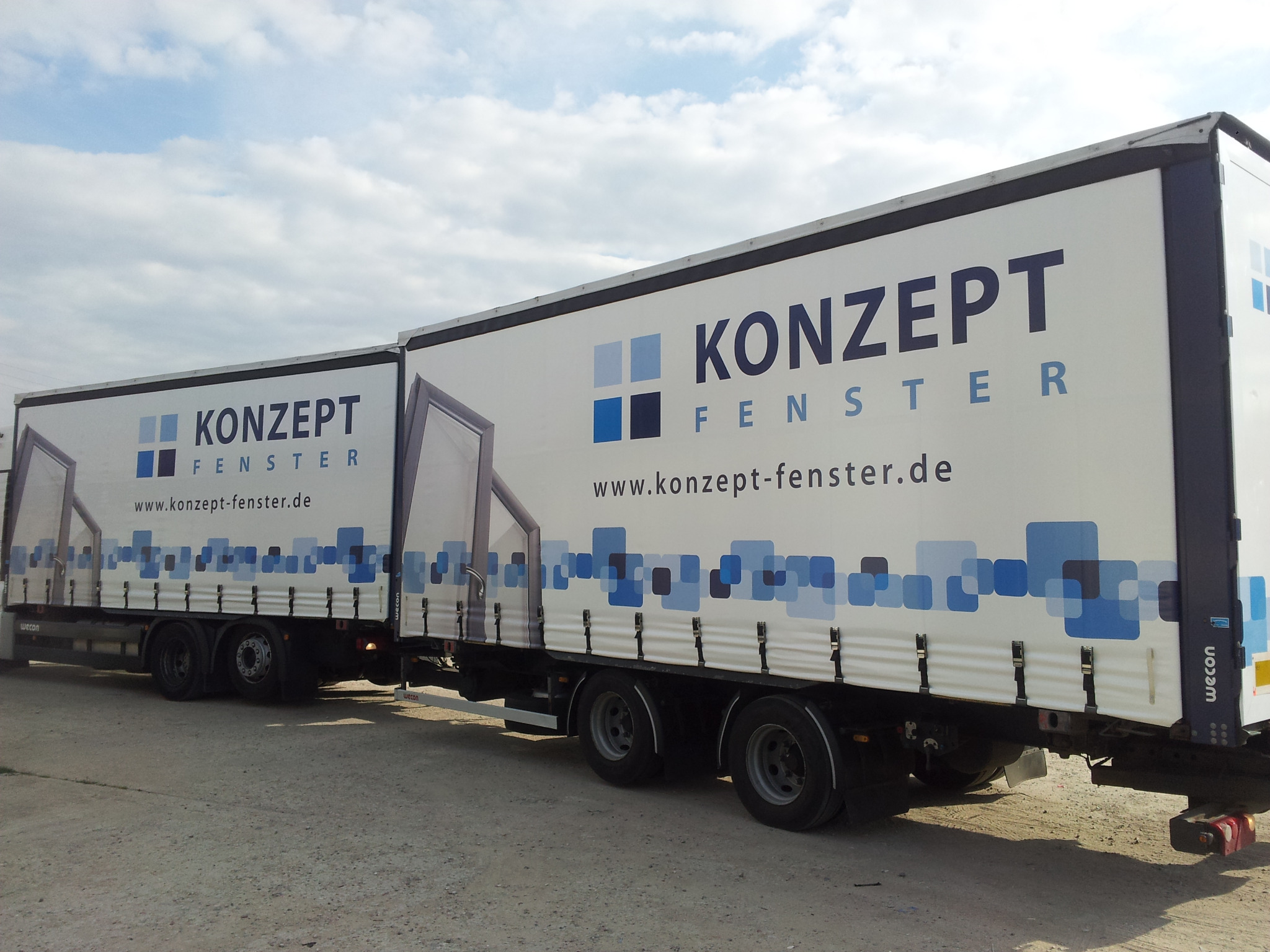 Dwa białe samochody ciężarowe z naczepami, na których widnieje logo firmy 'Konzept Fenster' i grafika okien. Naczepy z boku ozdobione są niebieskimi kwadratami. Na naczepach widnieje adres strony...