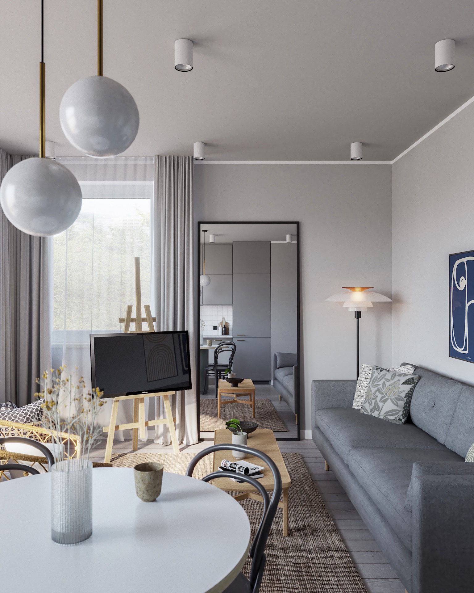 Jasne wnętrze salonu z szarą sofą, okrągłym stołem i lustrem odbijającym kuchnię. Na pierwszym planie wazon z kwiatami, w tle telewizor na sztaludze.