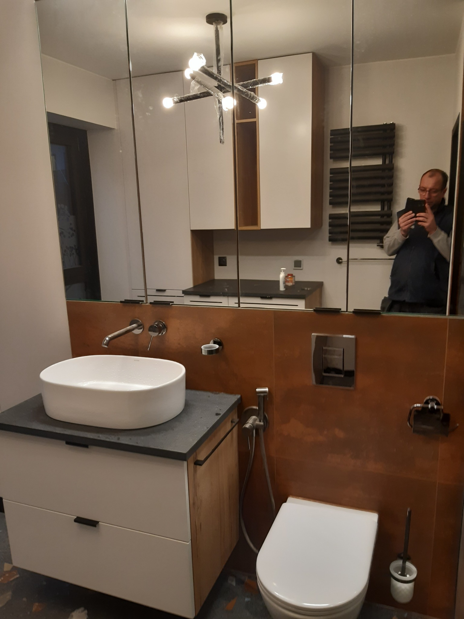 Nowoczesna łazienka z umywalką nablatową, toaletą podwieszaną i lustrem na całą ścianę, odbicie osoby robiącej zdjęcie w lustrze.