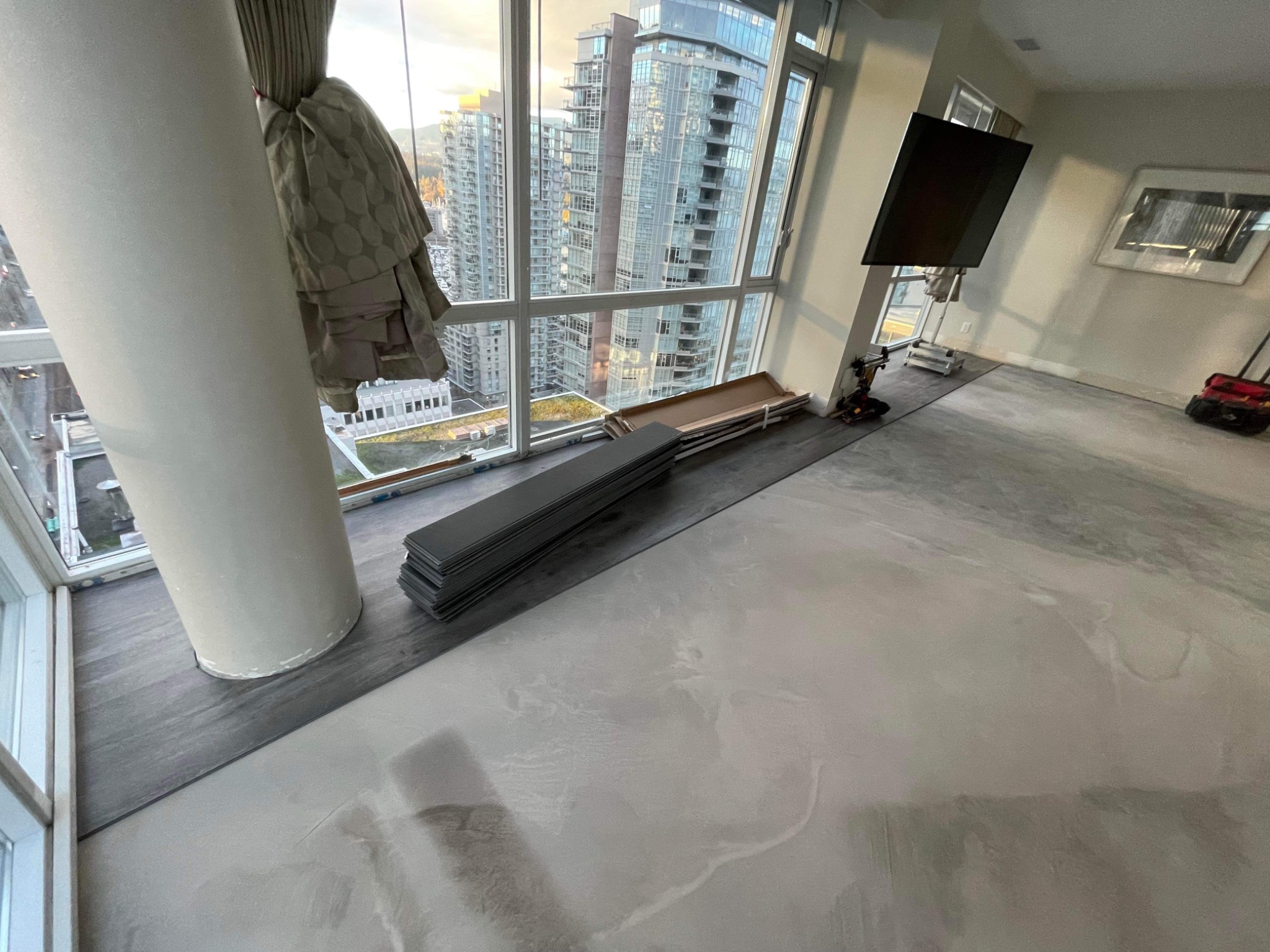 Układanie paneli podłogowych w apartamencie z widokiem na miasto; widoczne panele ułożone przy oknie oraz narzędzia do montażu.