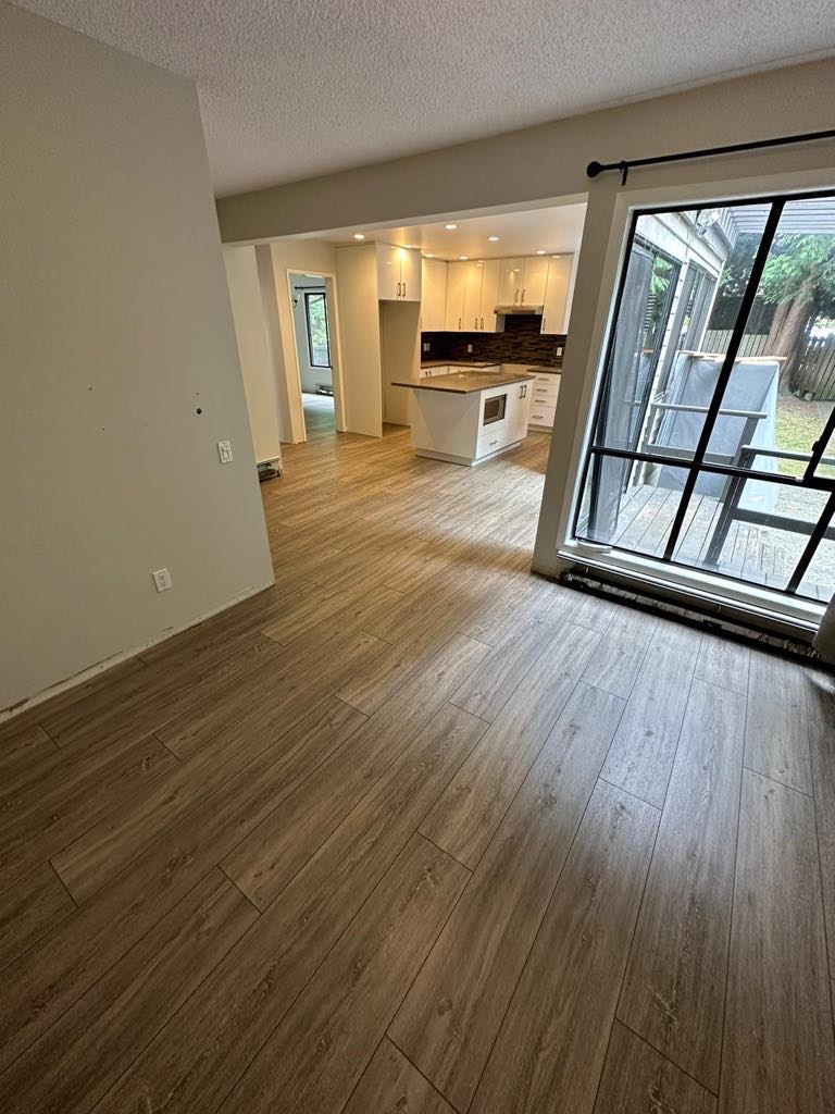 Ukończona podłoga z paneli imitujących drewno w jasnym salonie z widokiem na kuchnię i balkon.