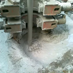 Wiertnica zagłębiająca się w ziemię, otoczona mieszaniną wody i urobku, widok z bliska na mechanizm wiertniczy.