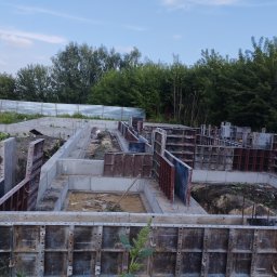 R-C BUD Robert Czuj - Fundamenty domu w trakcie budowy, widoczne szalunki i betonowe ściany fundamentowe na tle drzew i nieba.