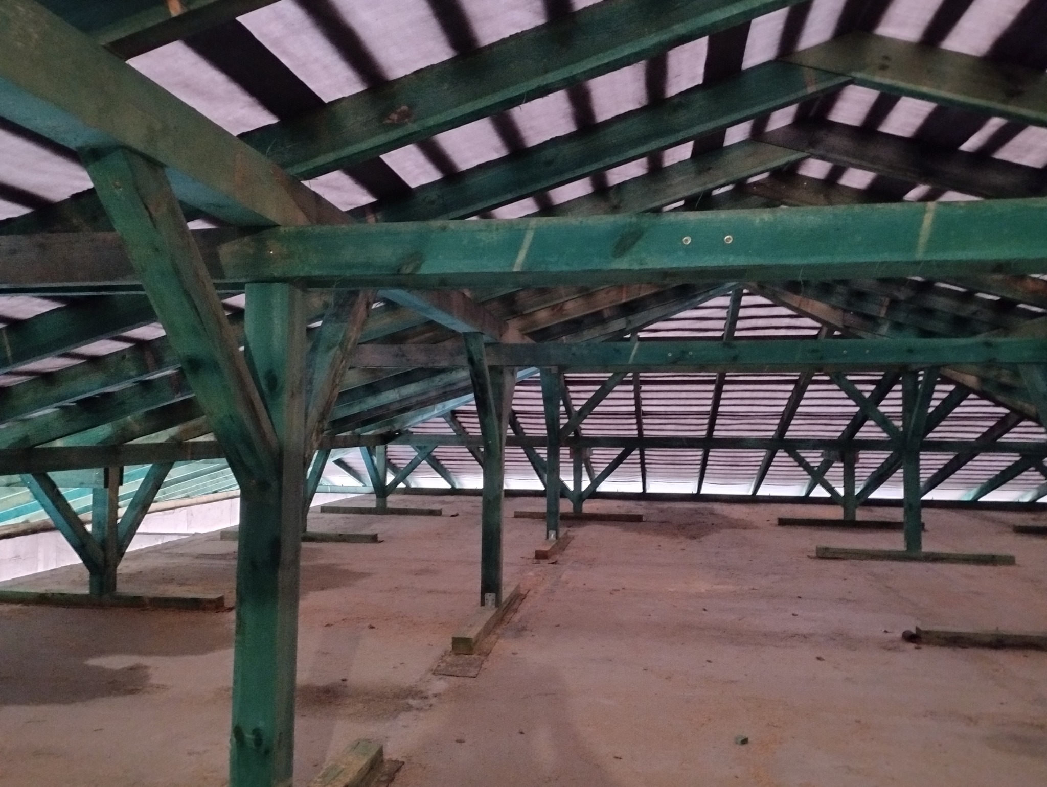 Konstrukcja drewniana dachu z zielonymi belkami nośnymi i membraną dachową widoczna od wewnątrz poddasza.