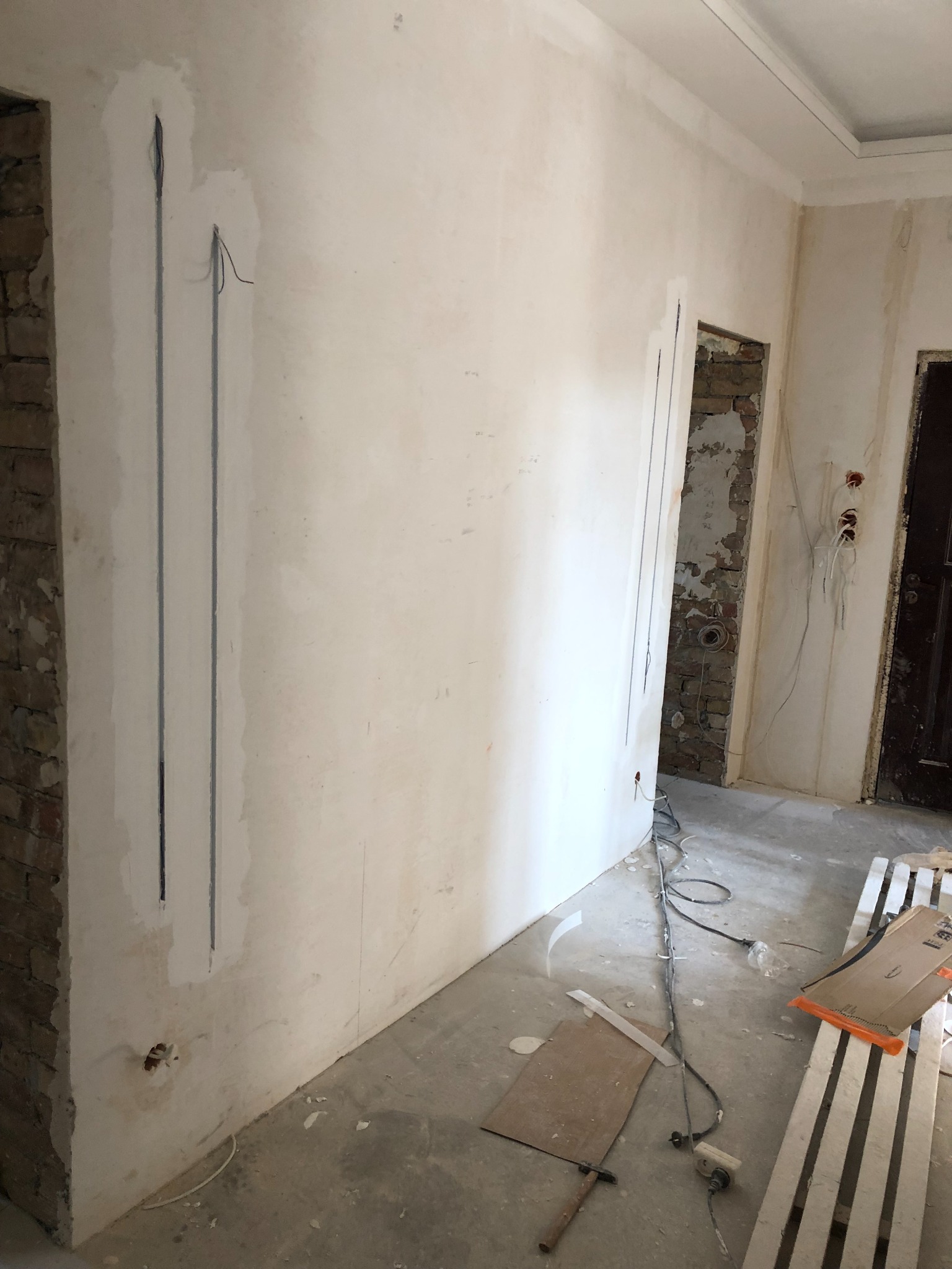 Ściana w trakcie przygotowywania pod instalację elektryczną, widoczne wyżłobione kanały na przewody, surowy tynk i fragmenty cegieł przy ościeżnicy.