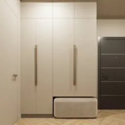 Wnętrze przedpokoju: zabudowana szafa w odcieniach beżu z długimi, smukłymi uchwytami, pufa tapicerowana pod szafą, parkiet w jodełkę oraz ciemnoszare drzwi wejściowe.