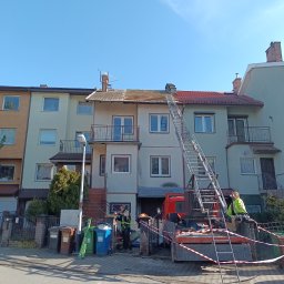 METAL-TRANS Mariusz Błoński - Ekipa na drabinie przy dachu budynku podczas prac. Widoczny samochód z drabiną, pracownicy w strojach roboczych i zabezpieczenia. Częściowo zdjęty dach.