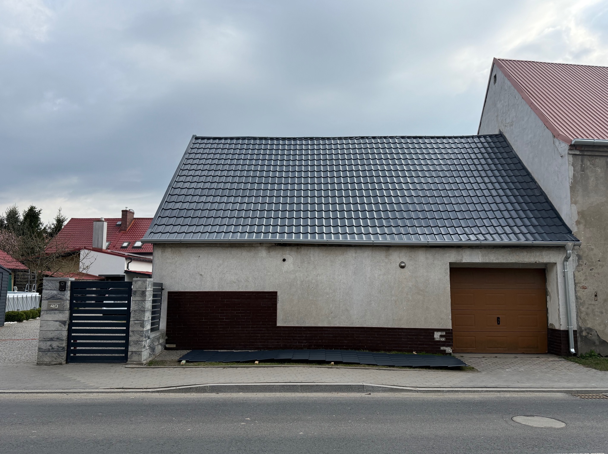 Nowy, grafitowy dach z dachówki ceramicznej na parterowym budynku z garażem, widok z ulicy w pochmurny dzień.