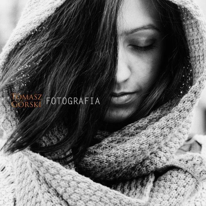 Portret kobiety w czarno-białej tonacji, z głową otuloną grubym, dzierganym szalem, włosy opadają na twarz, oczy zamknięte, spokojny wyraz twarzy.