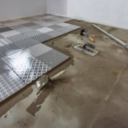 Vadym Smyrnyy - Układanie mozaiki z płytek podłogowych o różnych wzorach, widoczne narzędzia: poziomica, kielnia i młotek.