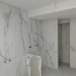 Vadym Smyrnyy - Wnętrze w trakcie wykańczania z marmurowymi płytkami na ścianach, widoczne wystające kable, fragment niedokończonej zabudowy i rury wodne.