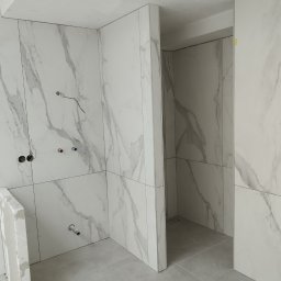 Vadym Smyrnyy - Wnętrze łazienki w trakcie wykańczania, widoczne płytki imitujące marmur na ścianach i podłodze, niezamaskowane przewody elektryczne i rury wodne, fragment ściany w stanie surowym.