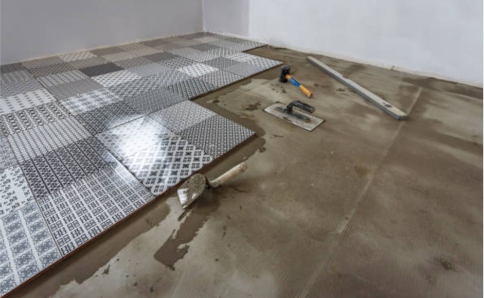 Układanie mozaiki z płytek podłogowych o różnych wzorach, widoczne narzędzia: poziomica, kielnia i młotek.