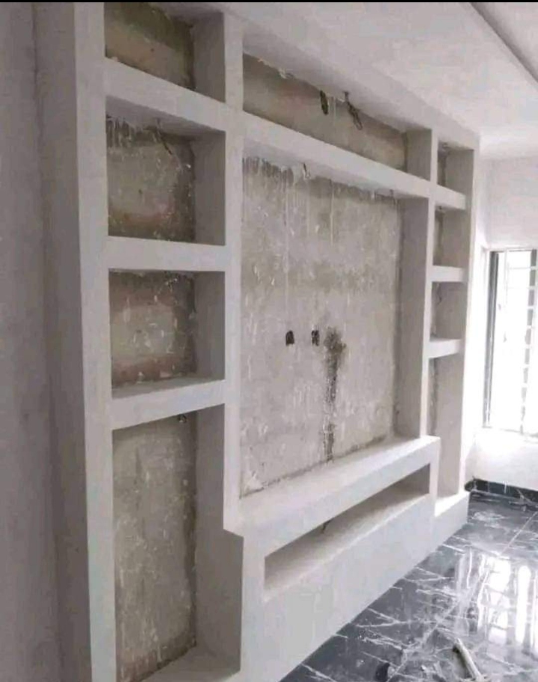 Ściana w trakcie tworzenia zabudowy z płyt karton gips, widoczne wnęki i półki, szpachlowane łączenia, surowy stan przed malowaniem, marmurowa posadzka.