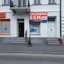 Fasada budynku z szyldami 'Akcesoria GSM', 'Doctor GSM Serwis i Naprawa' oraz 'Bukmacherskie Zakłady Sportowe', widok z ulicy.