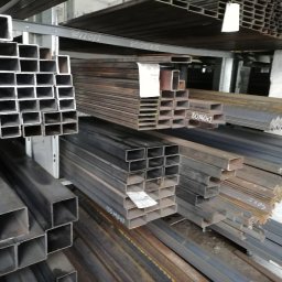 ogrodzenia, wyroby hutnicze, sklep spawalniczy - Ecolux - Składowane profile stalowe o różnych przekrojach, w tym kwadratowe i kątowniki, na metalowych regałach w magazynie.