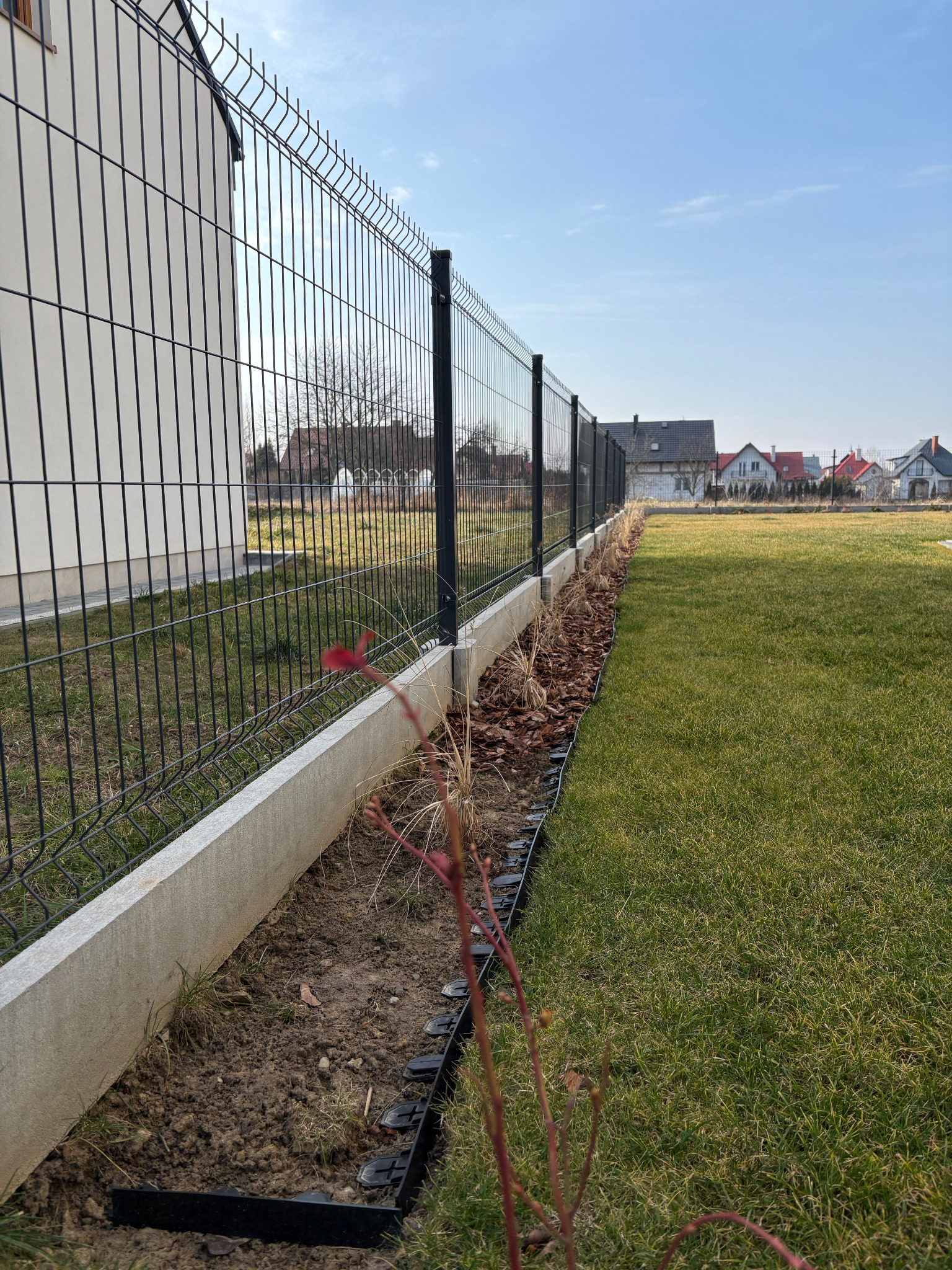 Nowoczesne ogrodzenie panelowe z podmurówką betonową w Orłach, widok na zadbany trawnik i domy w tle.