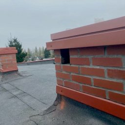 Artur Novikau - Wykończony komin z cegły z metalową obróbką na dachu pokrytym papą. W tle drugi komin i drzewa. Widok z góry, pochmurny dzień.