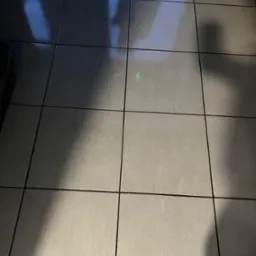 Błyszczące, jasnoszare płytki podłogowe z ciemnymi fugami, odbijające światło i cień