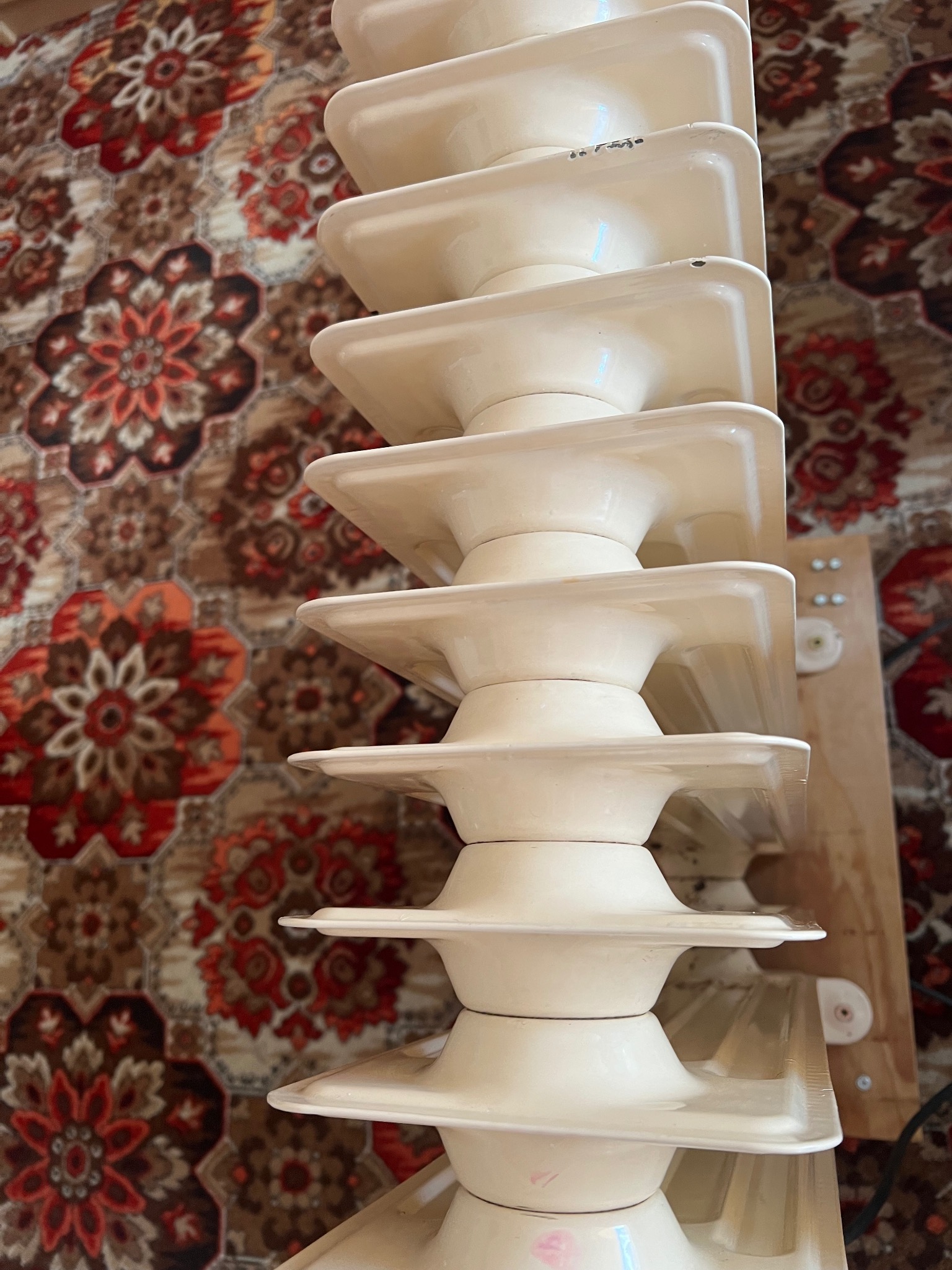 Biały, żeberkowy grzejnik na tle wzorzystego dywanu, widoczne drobne uszkodzenia farby.