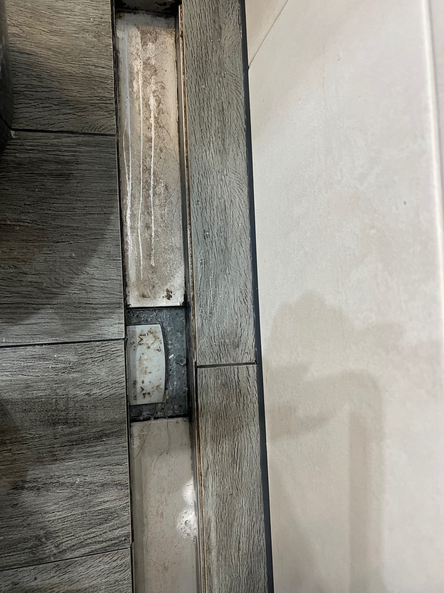 Szczegół ułożonej podłogi z płytek imitujących drewno, z widocznymi zabrudzeniami w szczelinach dylatacyjnych i przy listwie przypodłogowej, z bliska ukazujący potrzebę dokładnego doczyszczenia.