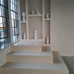 Minimalistyczne wnętrze z beżowymi ścianami, wnękami z dekoracyjnymi wazonami i schodkowym podestem, oświetlone przez duże okno z czarnymi szprosami.