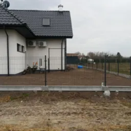 Montaż ogrodzenia panelowego z podmurówką betonową wokół domu, widoczne narzędzia i przygotowany teren.