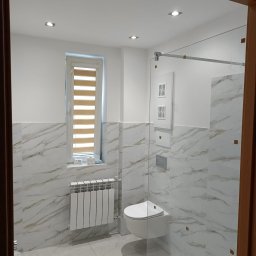 Usługi i Inwestycje Mateusz Janicki - Nowoczesna łazienka z marmurowymi płytkami, podwieszaną toaletą, grzejnikiem panelowym i kabiną prysznicową ze szklaną ścianką.