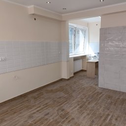 Usługi i Inwestycje Mateusz Janicki - Wykończona kuchnia z drewnopodobną podłogą, białymi płytkami metra na ścianie i beżowymi ścianami, widoczne gniazdka i oświetlenie sufitowe.