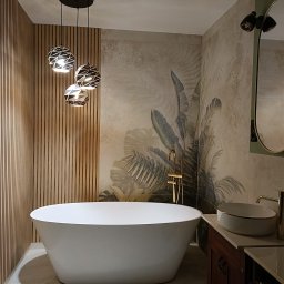 Usługi i Inwestycje Mateusz Janicki - Nowoczesna łazienka z wolnostojącą wanną, armaturą w kolorze złota, płytkami z motywem roślinnym i drewnianymi lamelami na ścianie, oświetlona trzema designerskimi lampami wiszącymi.
