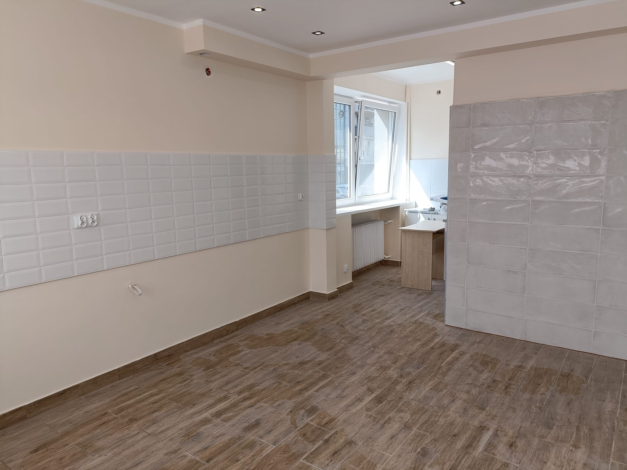 Wykończona kuchnia z drewnopodobną podłogą, białymi płytkami metra na ścianie i beżowymi ścianami, widoczne gniazdka i oświetlenie sufitowe.