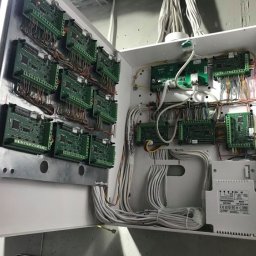 Force Design sp. z o.o. - Otwarta biała skrzynka rozdzielcza z licznymi zielonymi płytkami drukowanymi i kablami, widoczny transformator NOVA AWT500 na dole.