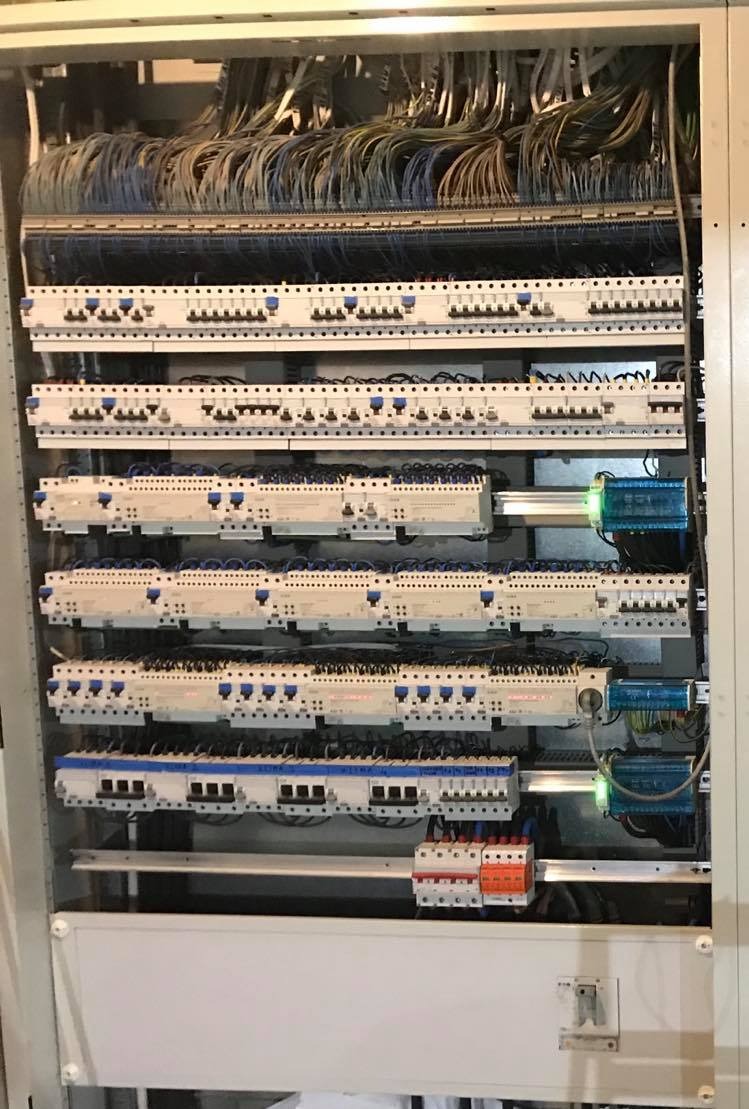 Rozdzielnica elektryczna z licznymi przewodami, zabezpieczeniami i modułami, widoczne połączenia i okablowanie wewnątrz szafy.