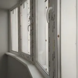 Zamontowane okna PCV marki Blitz z białymi ramami i klamkami, widoczne z bliska od strony wnętrza, z widocznymi naklejkami producenta na profilach.