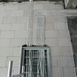 Rozprowadzenie przewodów elektrycznych w peszlach, ułożonych wzdłuż ściany z betonu komórkowego, w trakcie prac instalacyjnych w Ostródzie. Widoczna metalowa szafka rozdzielcza i fragment rusztowania.