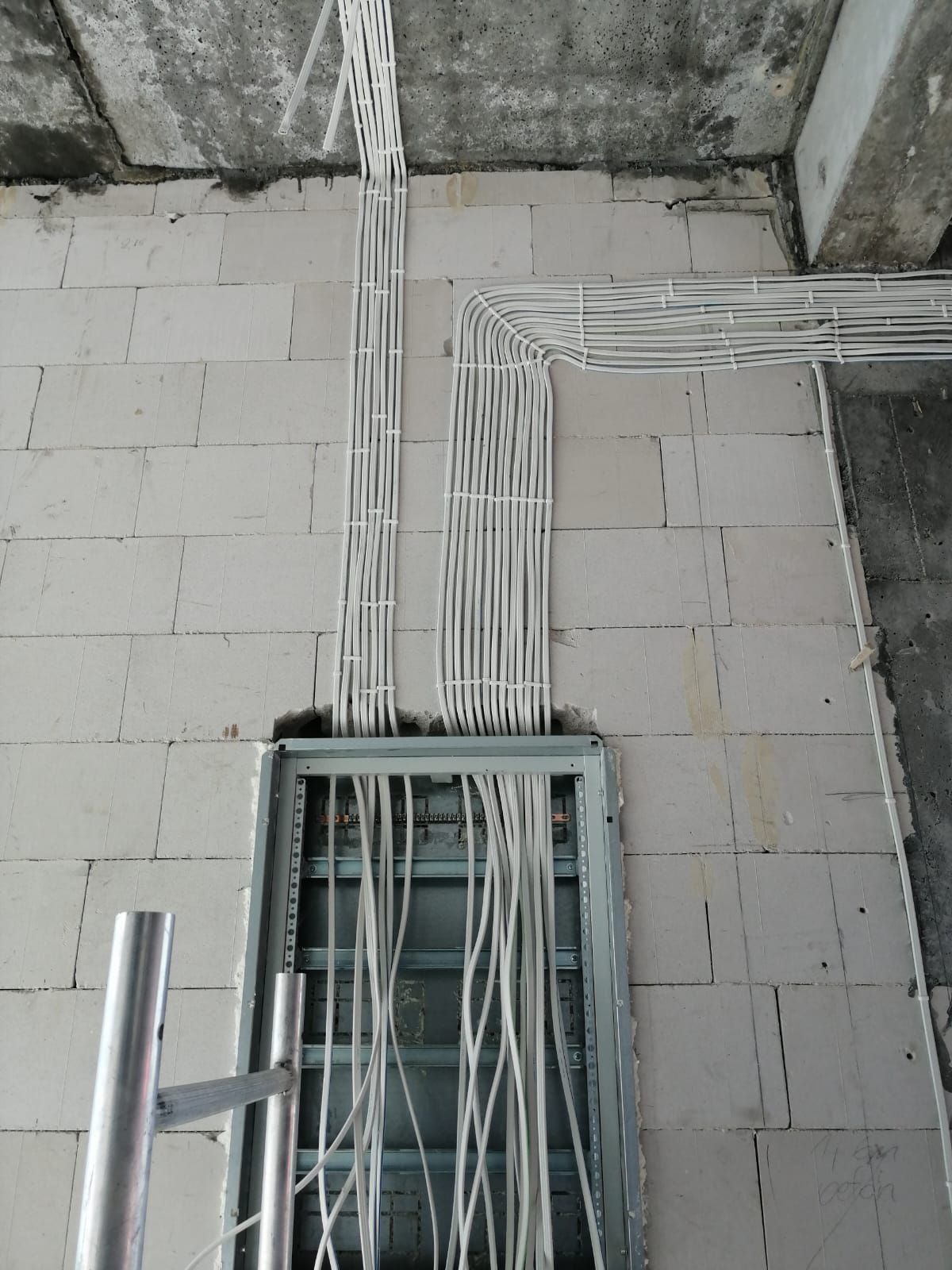 Rozprowadzenie przewodów elektrycznych w peszlach, ułożonych wzdłuż ściany z betonu komórkowego, w trakcie prac instalacyjnych w Ostródzie. Widoczna metalowa szafka rozdzielcza i fragment rusztowania.