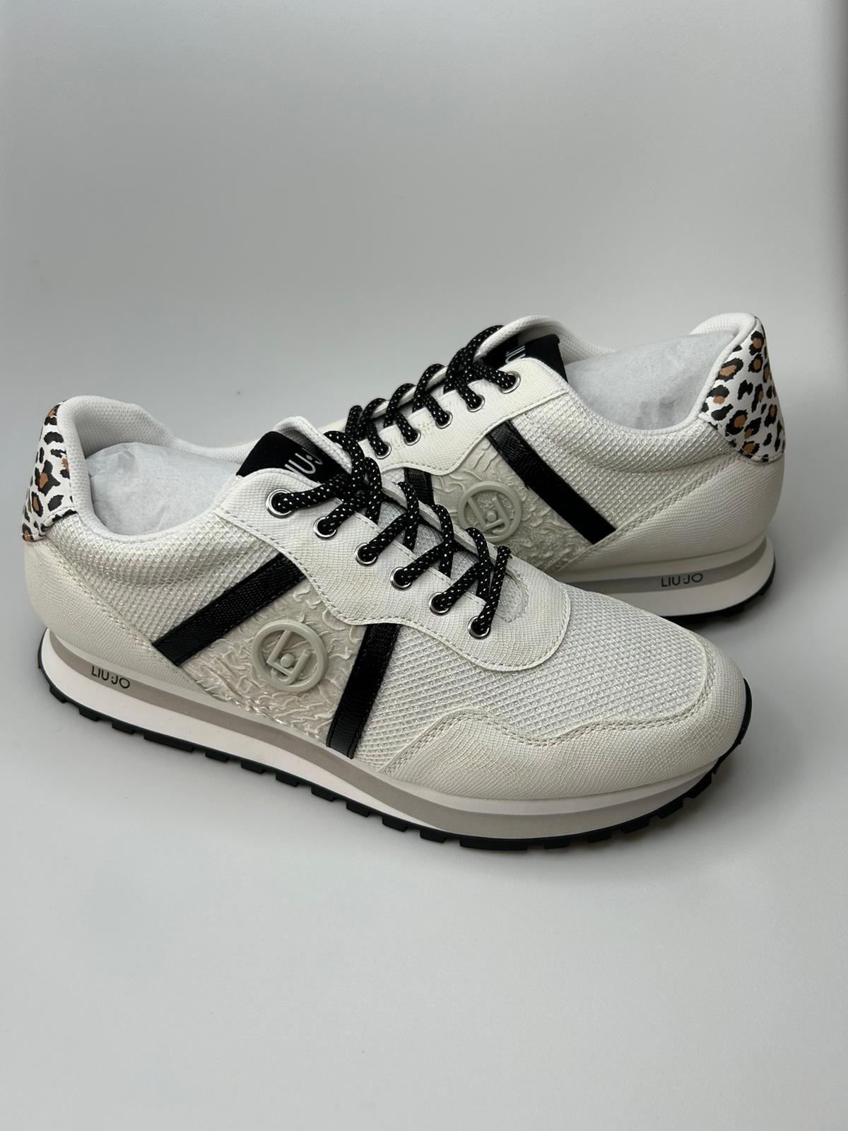 Para białych sneakersów Liu Jo z czarnymi sznurówkami, lampasem i wzorem w panterkę na zapiętku, na białym tle.