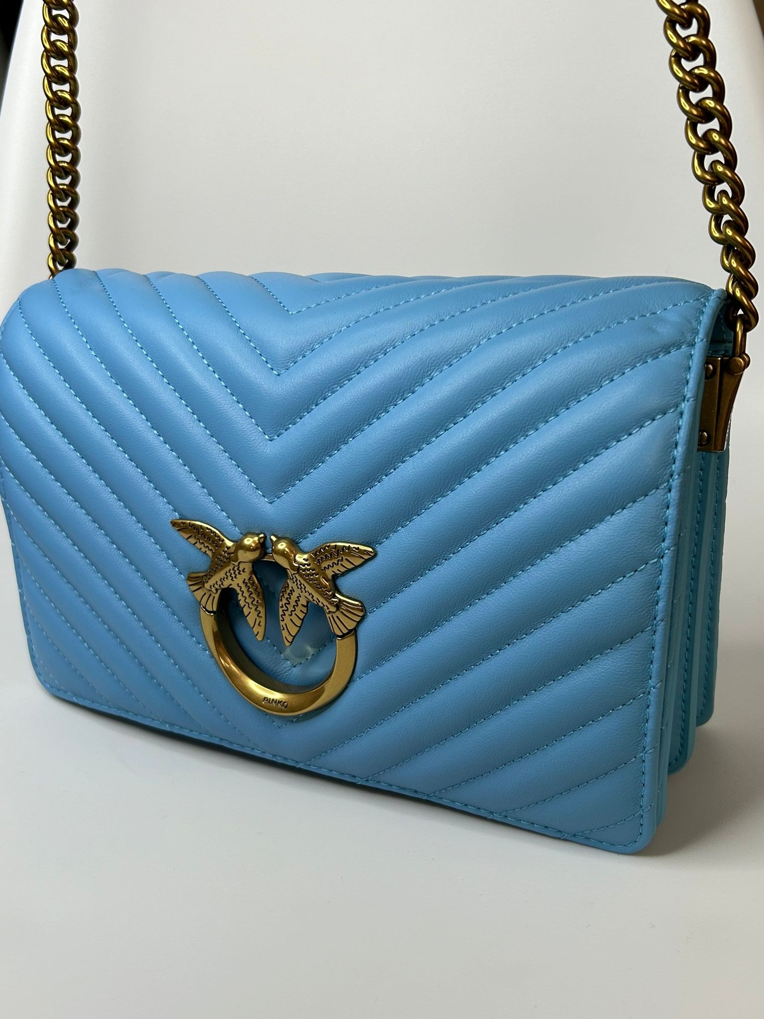 Błękitna pikowana torebka damska z złotym łańcuszkiem i logo z dwoma ptakami.