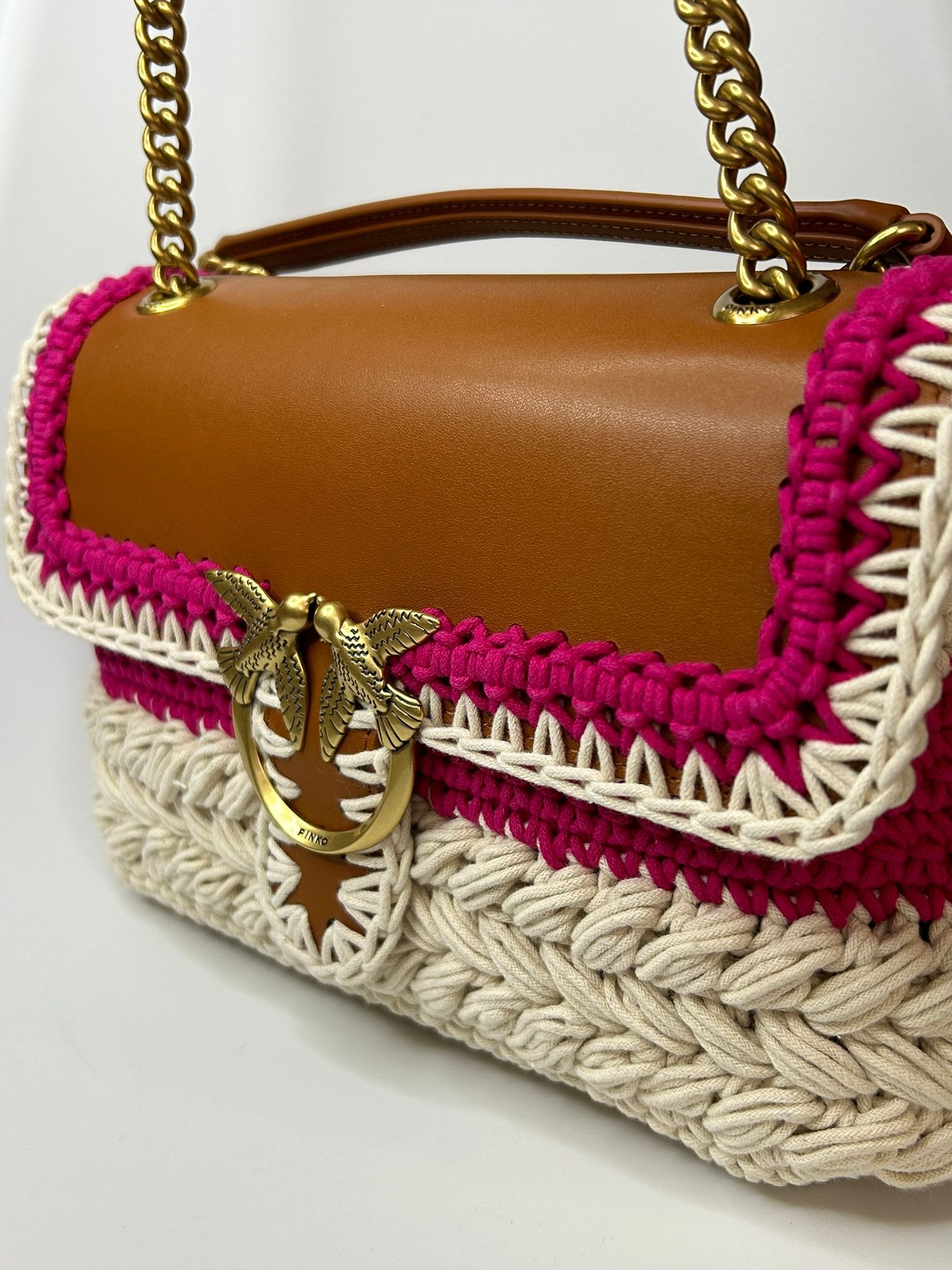 Brązowa torebka z elementami szydełkowymi w kolorze kremowym i różowym, zdobiona złotym logo z ptakami.