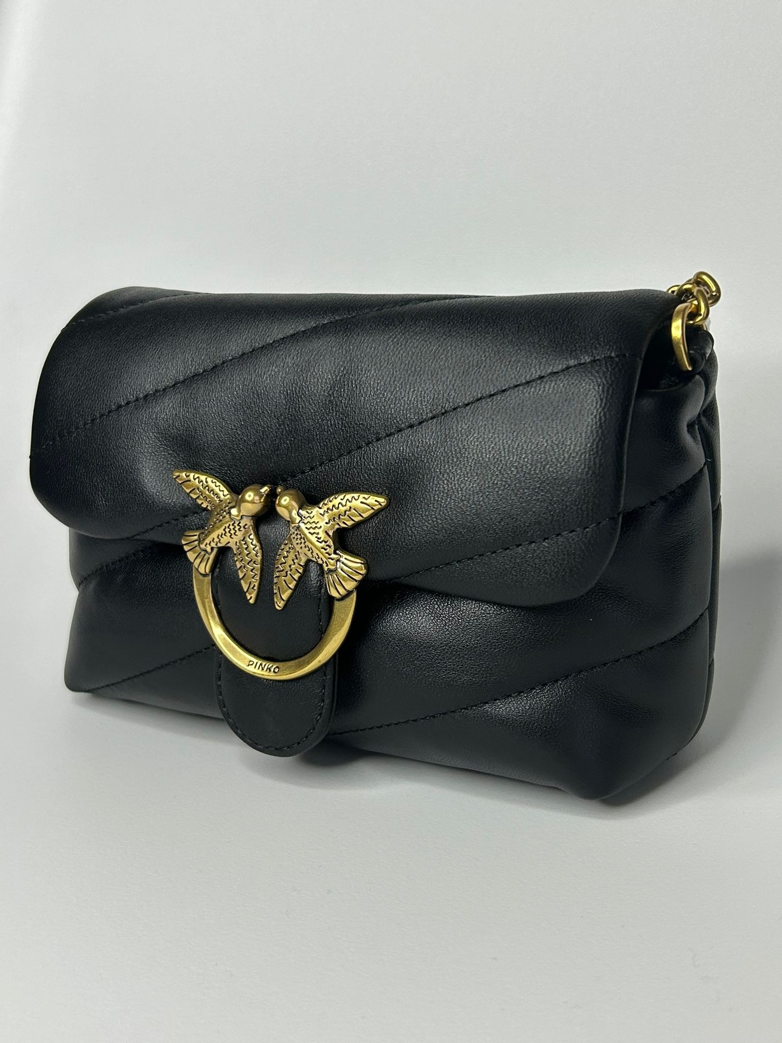Czarna pikowana torebka marki Pinko z charakterystycznym złotym zapięciem w kształcie dwóch ptaków.