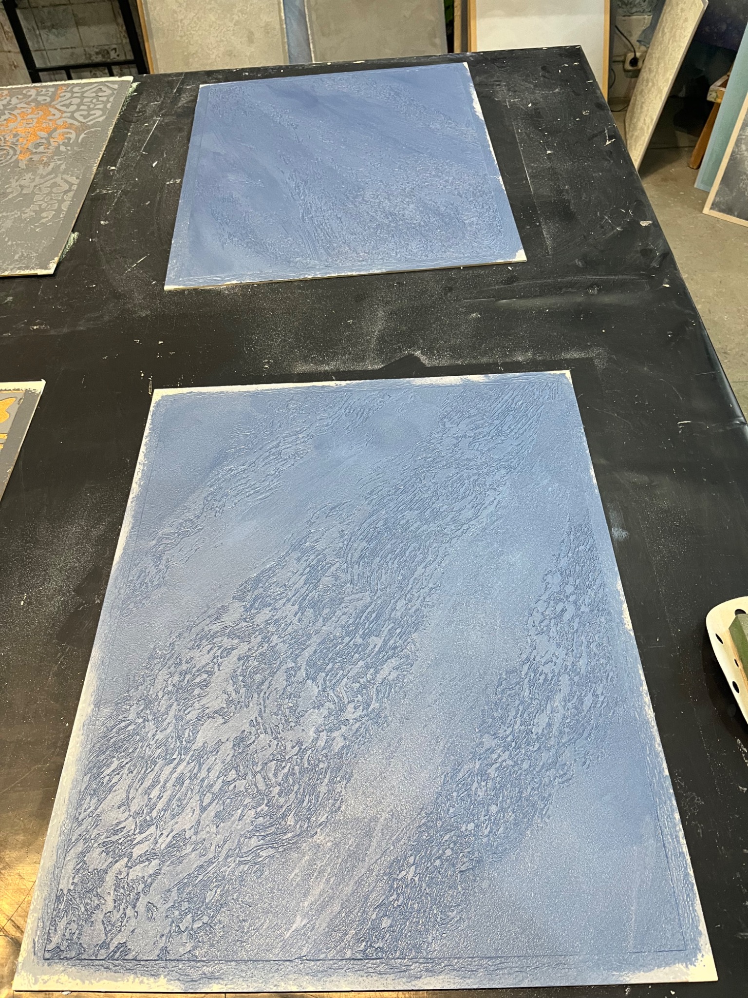 Próbki tekstur dekoracyjnych w odcieniach błękitu na czarnym stole warsztatowym, prezentujące różne techniki wykończeniowe.