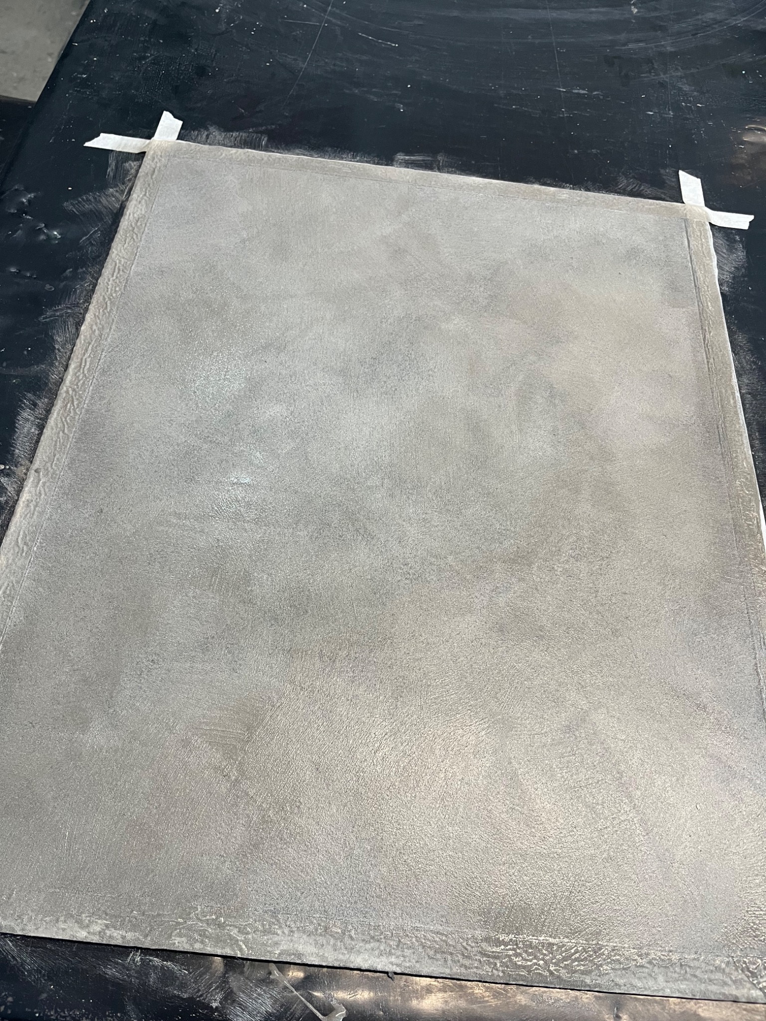 Świeżo pomalowana, szara powierzchnia zabezpieczona taśmą malarską na brzegach, widoczne ślady pędzla i faktura farby.