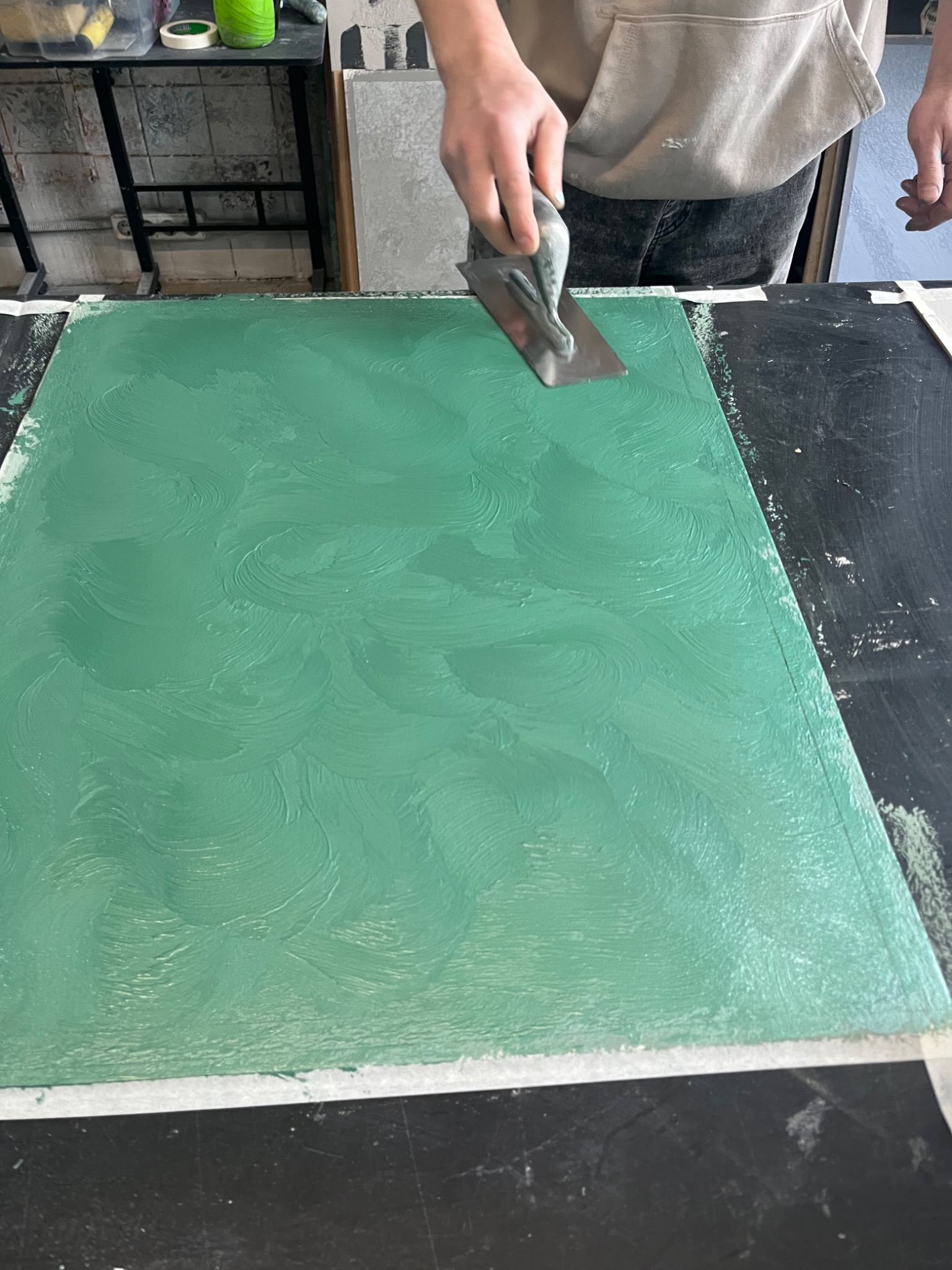 Nakładanie zielonej farby dekoracyjnej pacą na powierzchnię, widoczne ślady pociągnięć i struktura farby.