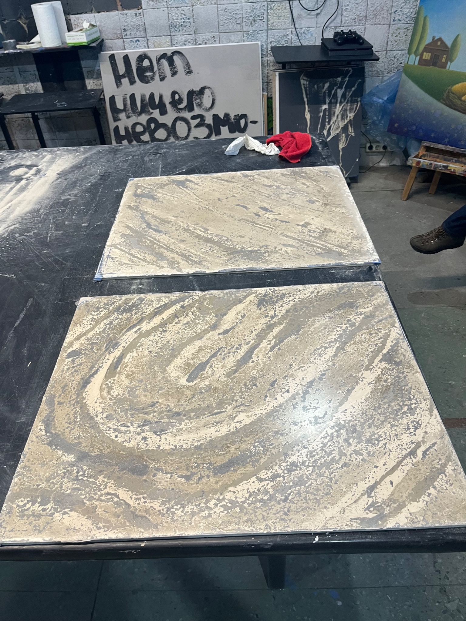Dwa kwadratowe panele dekoracyjne z efektem marmuru w odcieniach beżu i szarości, prawdopodobnie przygotowywane do montażu w Warszawie, leżą na czarnym stole w warsztacie.