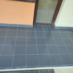 Balkon z szarą, błyszczącą terakotą ułożoną w regularną siatkę, widok z góry na narożnik balkonu z oknem i pomarańczową ścianą.